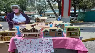 La señora busca ganarse la vida por medio de pequeñas casitas de cartón a cambio de lo que las personas le puedan ofrecer.