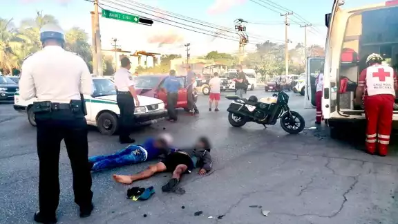 El motociclista y su acompañante terminaron en el pavimento tras el impacto contra el taxi en Cancún, por lo que fueron valorados por paramédicos El motociclista y su acompañante terminaron en el pavimento tras el impacto contra el taxi en Cancún, por lo que fueron valorados por paramédicos