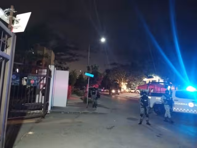 Elementos estatales y federales resguardan una plaza comercial frente al fraccionamiento Xcacel, donde agentes ministeriales realizan diligencias al interior de varios locales