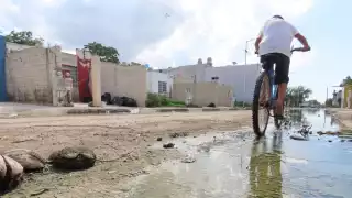 Niños transitan por las aguas residuales en bicicleta, en Kanasín